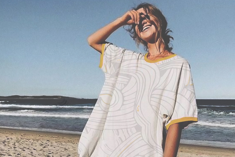 Girl smiling close to the ocean wearing long printed tee shirt.