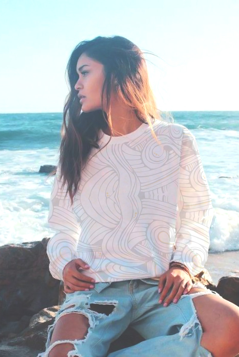 Long haired asian woman sitting on a rock, close to the ocean. Wearing printed sweatshirt.