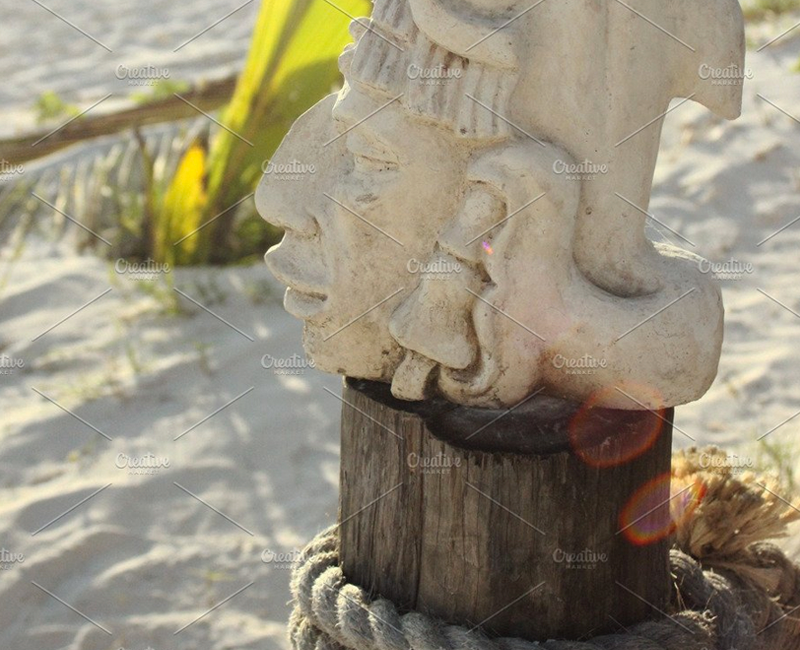 Native American people as a statue at the beach, white sand, sunny day, on top of a wooden bloc with rope around it. Cancun, Mexico.