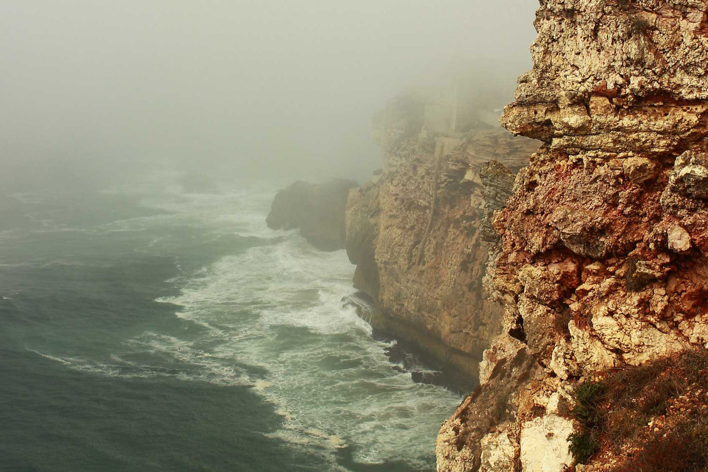 Rock formation, coastal side, facing the ocean. Nature photo, rock with red tones, fog surrounding it. Waves crashing. Photo sold on Creative Market.
